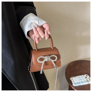 Detail of a brown leather mini crossbody bag featuring a sparkling silver rhinestone bow