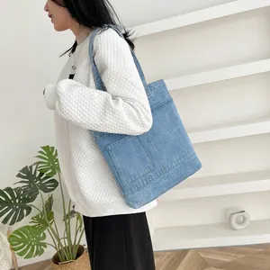 Detail of light blue denim tote bag with functional front pockets and contrast stitching