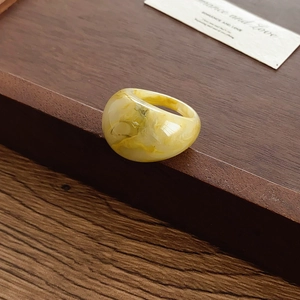 Détail d'une bague bombée en résine avec texture marbrée jaune et blanche sur bois
