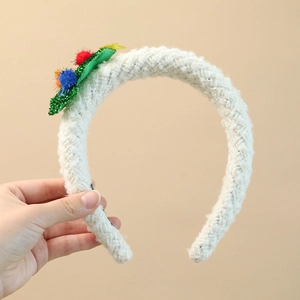 Detail of white knit headband with colorful plush balls and green leaf ornaments