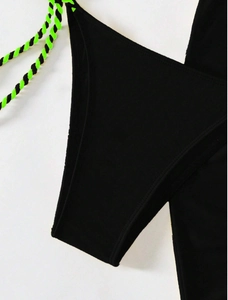 Close-up of black bikini bottoms with neon green braided side ties and elastic fabric