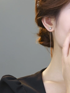 Macro shot of silver tassel earrings with star zircon studs worn by a female model