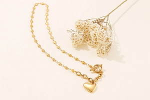 Detail of gold heart link necklace with heart pendant and T-bar toggle clasp on beige background