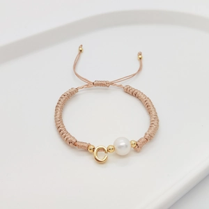 Detail of hand-woven cord bracelet with a pearl and golden letter C pendant charm