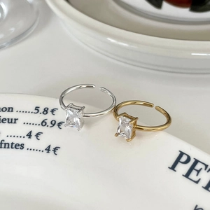 Detail of square zircon adjustable open rings in gold and silver on white ceramic plate