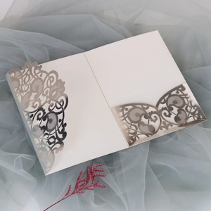 Detailed laser-cut silver patterns on ivory wedding invitation sleeve with floral mesh
