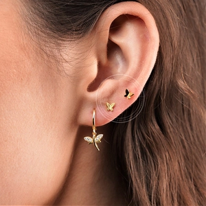 Close-up of golden butterfly earrings with zircon crystals worn by a female model
