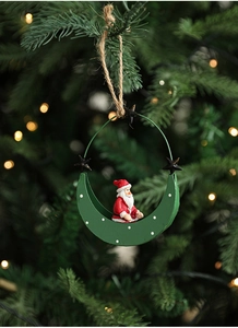Detail of a green crescent moon Christmas ornament with Santa Claus hanging on a pine tree