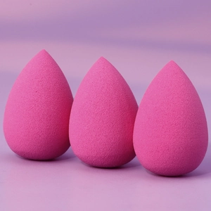Detailed view of three rose pink teardrop-shaped makeup sponges on purple background