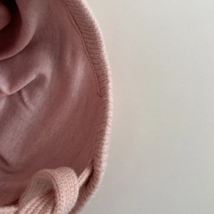 Close-up of pink knitted baby bonnet showing fine stitching and soft yarn texture