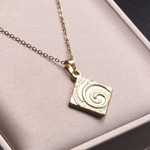 Close-up of 18k gold plated square swirl pendant on a soft beige jewelry box cushion