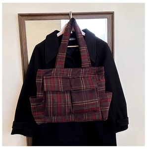 Detail of red and green plaid tote bag featuring multiple pockets and warm wool texture