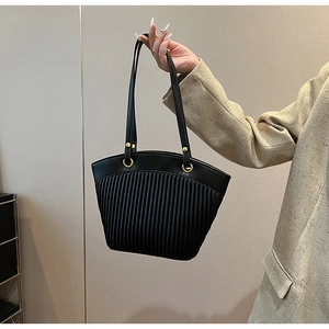 Detail of black tote bag with vertical pleats and golden metal ring hardware