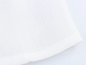 Detailed close-up of white cotton linen fabric with tassel fringe and neat hem stitching