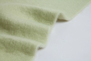 Close-up of soft thick light green mohair fabric with fine texture and warm fuzzy finish