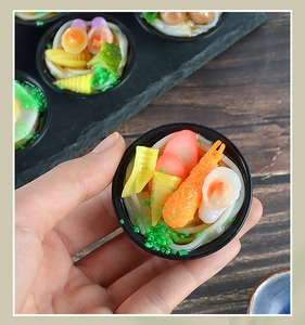 Detailed macro view of a miniature ramen bowl model with shrimp and corn on a wooden desk