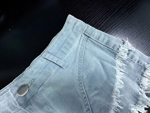 Dettaglio di pantaloncini di jeans a vita alta con bordi sfilacciati e bottone argento