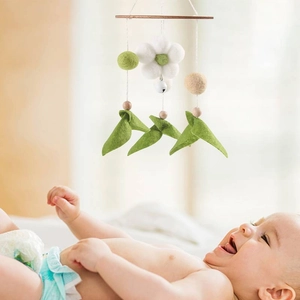 Close-up of baby crib mobile with felt flowers and wooden bar above a smiling infant