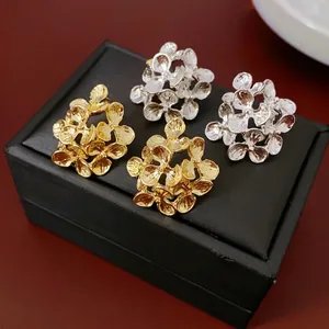 Golden and silver textured floral stud earrings displayed on a black jewelry box