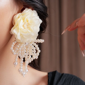 Detailed close-up of a large cream floral earring with elegant white pearl tassels