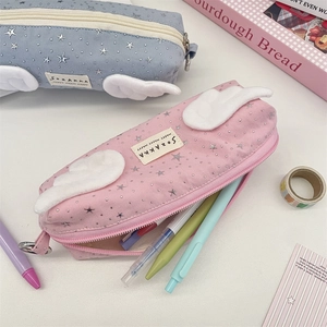 Close-up of canvas pencil cases with star patterns and plush wings holding colorful pens