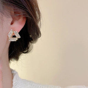 Detailed close-up of geometric gold-plated triangle stud earrings with shiny zircons on ear