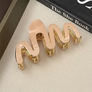 Detailed view of wave-shaped golden metal hair claw with nude pink resin finish