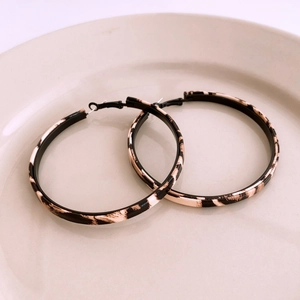 Close-up of leopard print hoop earrings with black metal hooks on a beige ceramic tray