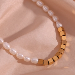 Macro shot of white pearls and golden cube beads on a luxury champagne satin background