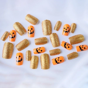 Unghie finte per Halloween con facce di zucca arancioni e glitter dorati brillanti