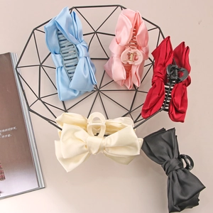 Large satin bow hair claws in five colors including pink and blue displayed in a metal basket