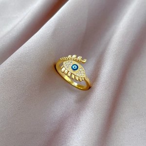 Close-up of gold evil eye ring with blue pupil and pavé crystals on pink silk background