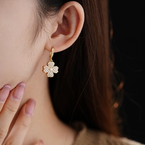 Close-up of gold clover earrings with pearls and zircons worn by a model