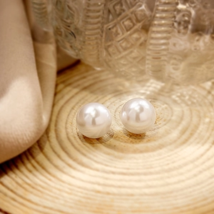 Macro detail of round white pearl earrings on minimalist natural wood display