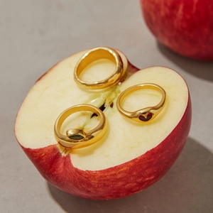 Detailed view of three gold zircon rings with heart stones placed on a fresh red apple