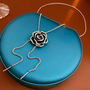 Close-up of black camellia pendant necklace with white crystals on a blue jewelry box