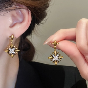 Detailed view of vintage gold fleur-de-lis earrings with centered white zircon stone