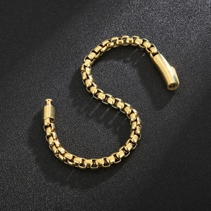Macro detail of golden stainless steel box chain bracelet on a black textured background