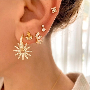 Macro shot of gold sun pendant earrings and studs set with white cubic zirconia