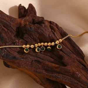 Close-up of 18K gold plated stainless steel anklet with green gemstone on wood
