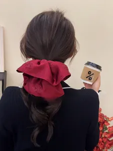 Detailed view of burgundy satin scrunchie with rose embroidery worn on dark hair
