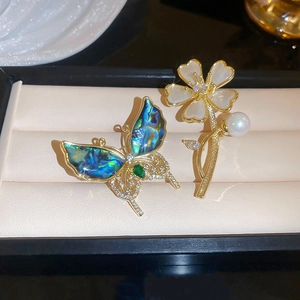Vue détaillée d'une broche papillon et fleur dorée à l'or fin avec nacre et zircons