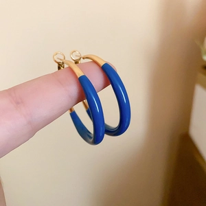 Close-up of golden C-shaped hoop earrings with royal blue glaze finish held by hand