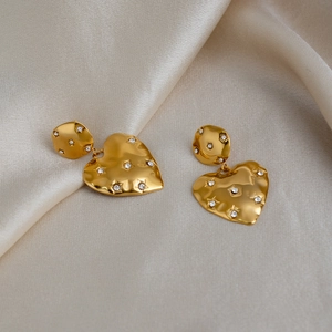 Detail of 18k gold plated heart earrings with sparkling rhinestones on champagne satin
