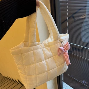 Close-up of a white quilted puffer tote bag featuring a pink plaid bow charm detail