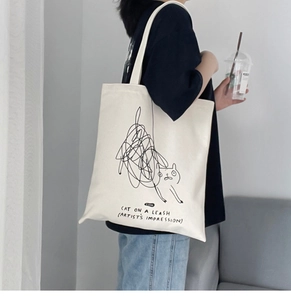 Close-up of minimalist cat doodle art and black text on a cream canvas tote bag