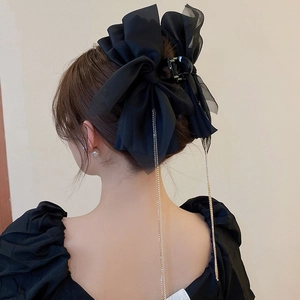Détail d'une pince à cheveux à nœud noir avec de longs glands métalliques fins