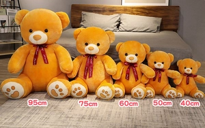 Multiple sizes of plush teddy bears in bright orange with Just for you red ribbons