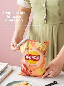 Close-up of cute cat paw sealing clip securing a potato chip bag on marble table