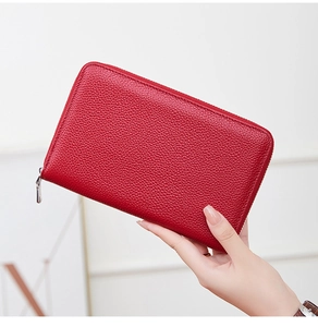 Detail of red pebbled leather long wallet with silver zipper held in hand for texture